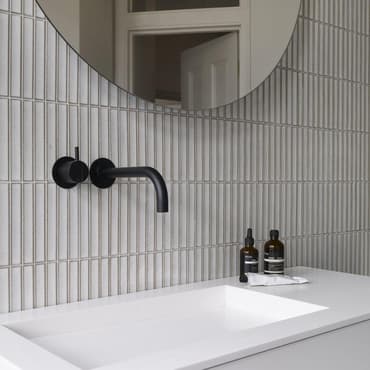 Carrelage uni gris clair avec joints contrastants dans une salle de bains épurée sur fond de robinetterie noire et accessoires de toilette