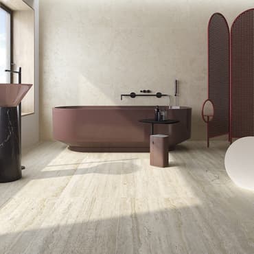 Carrelage effet béton beige nuancé dans une salle de bain moderne aux éléments bordeaux et noirs, avec baignoire ovale et miroir rond