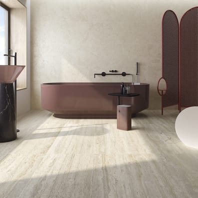 Carrelage effet béton beige nuancé dans une salle de bain moderne aux éléments bordeaux et noirs, avec baignoire ovale et miroir
