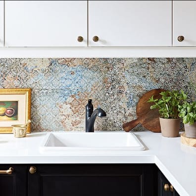 Carrelage effet tissu beige avec motifs multicolores 50x100 cm sur un mur de cuisine, meubles blancs et comptoir noir, touches d