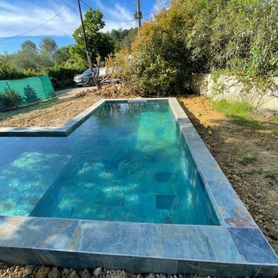 Carrelage pierre multicouleur nuances de gris et bleu 30x60 cm sur bord de piscine extérieure entourée de végétation