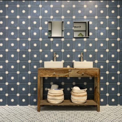 Carreau de ciment bleu à motif étoile blanc dans une salle de bain, murs et sol assortis, meuble en bois avec vasques, paniers e