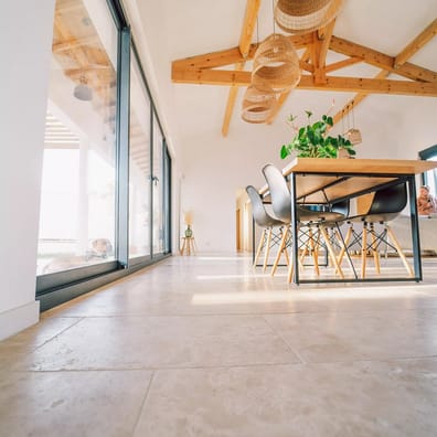 Carrelage effet pierre beige sans motifs dans un salon lumineux aux poutres en bois et mobilier moderne avec chaises noires et t