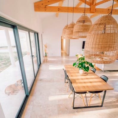 Carrelage effet pierre beige sans motifs dans un salon lumineux aux poutres en bois et mobilier moderne avec chaises noires et t