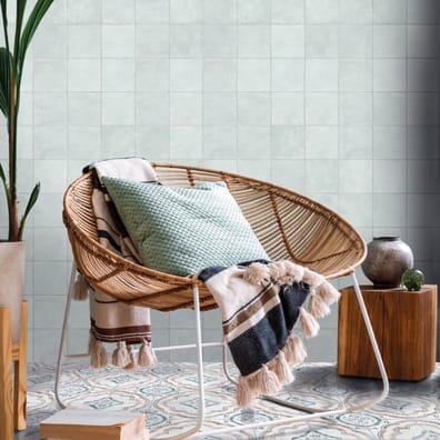 Carreau de ciment multicouleur motifs floraux verts et beiges 15x15 cm dans une pièce tons neutres avec chaise en osier coussins