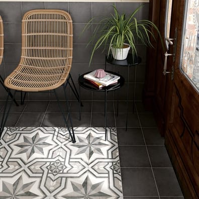 Carreau de ciment anthracite motifs étoilés 20x20 cm dans un salon avec murs gris et mobilier en rotin