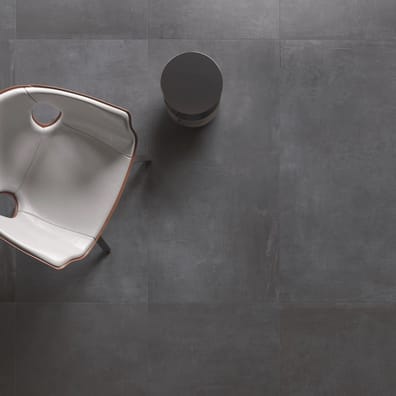 Carrelage effet ciment noir uni 60x60 cm dans un intérieur avec fauteuil design gris et table ronde noire épurée