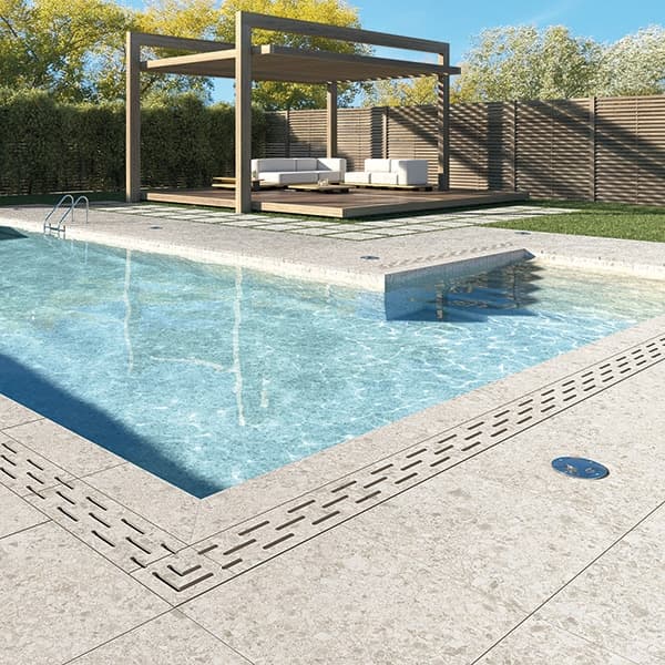 Terrazzo beige 60x60 cm sur une terrasse avec piscine bleue, herbe verte, salon de jardin beige et pergola en bois