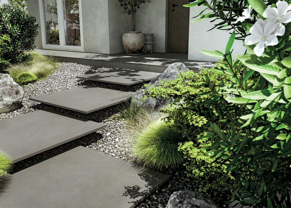 Carrelage effet pierre gris uni 60x60 cm dans un jardin avec galets, verdure et éléments décoratifs