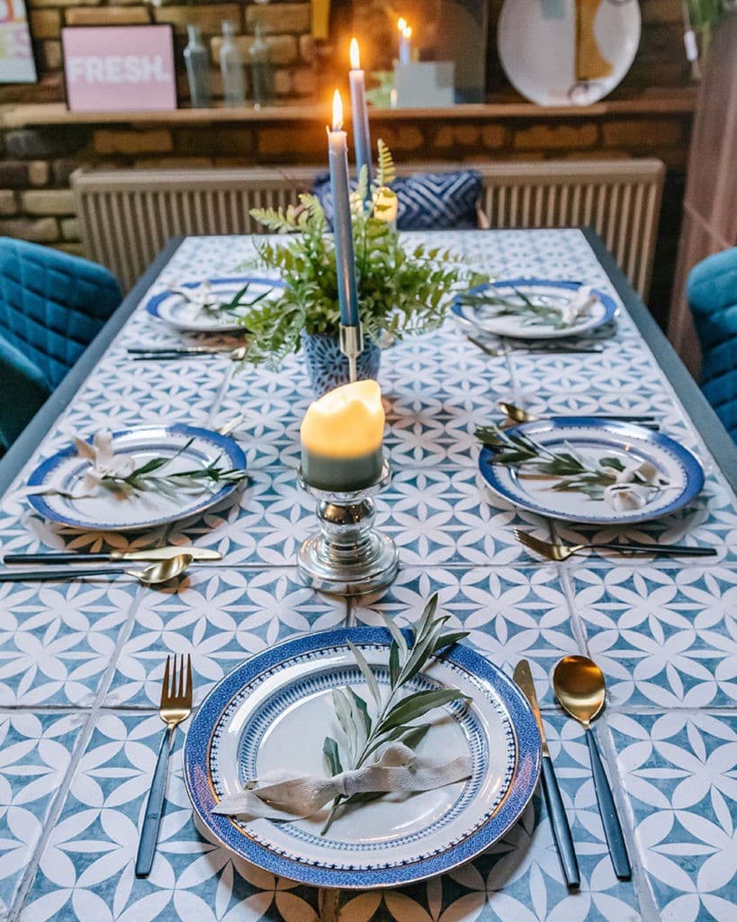 Carreau de ciment bleu avec motifs géométriques blancs 20x20 cm dans une salle à manger aux tons bleus et blancs avec table dressée et bougies