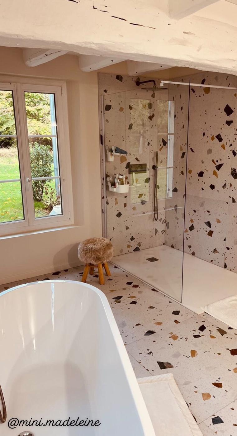 Carrelage Terrazzo blanc avec éclats multicolores 60x60 cm dans une salle de bain beige baignoire blanche et tabouret en bois