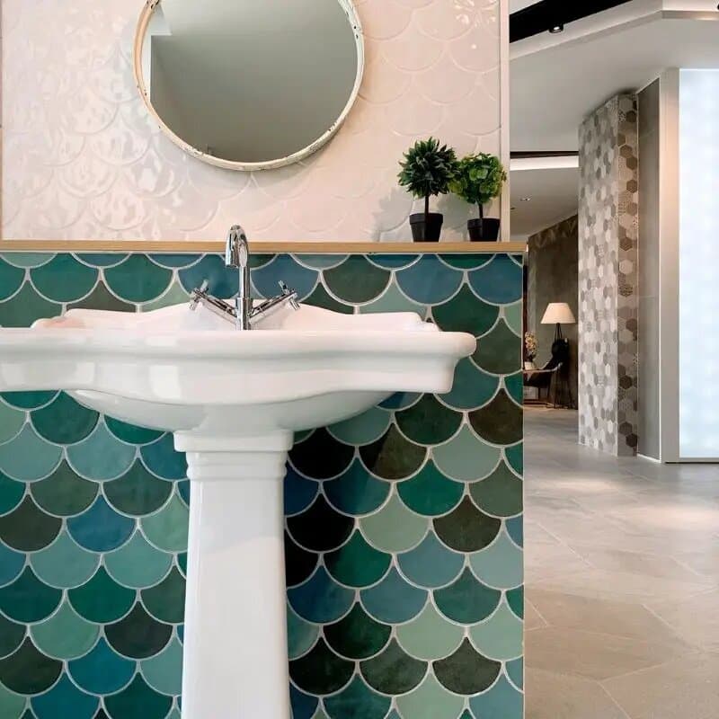 Carrelage uni vert écailles 30x30 cm sur un mur de salle de bain tons blancs lavabo colonne miroir rond plantes