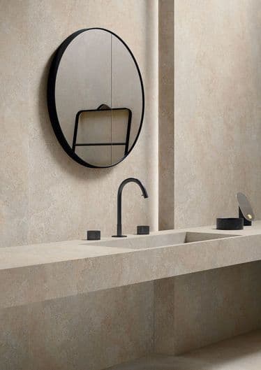 Carrelage effet pierre beige uni 60x60 cm dans une salle de bain ton sur ton avec lavabo et robinetterie modernes, miroir rond noir