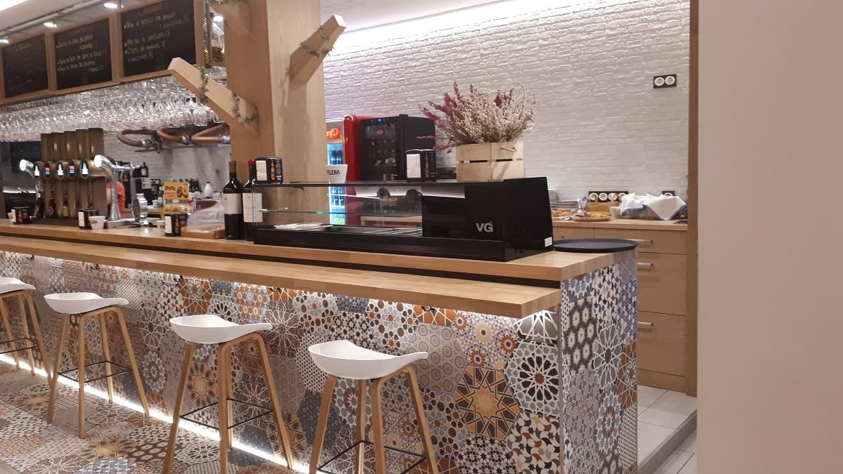 Carreau de ciment terracotta avec motifs géométriques 30x30 cm sur un bar dans une caféterie aux tons bois et blancs, détails de décoration florale