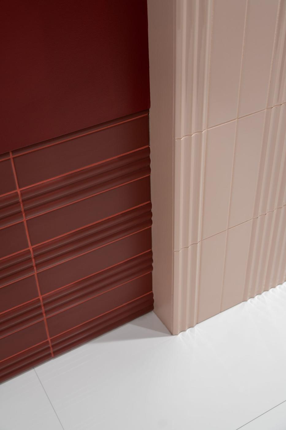 Carrelage uni rouge avec textures sur mur juxtaposé à des carreaux beige dans une ambiance de salle épurée aux tons doux
