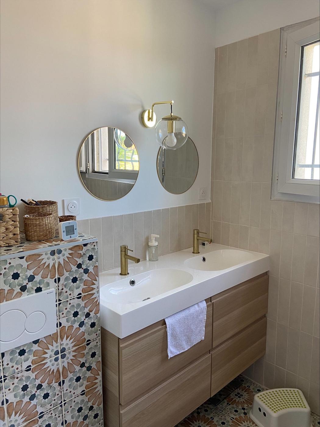 Carreau de ciment terracotta avec motifs floraux 20x20 cm dans une salle de bain beige miroirs ronds luminaire doré meuble bois clair