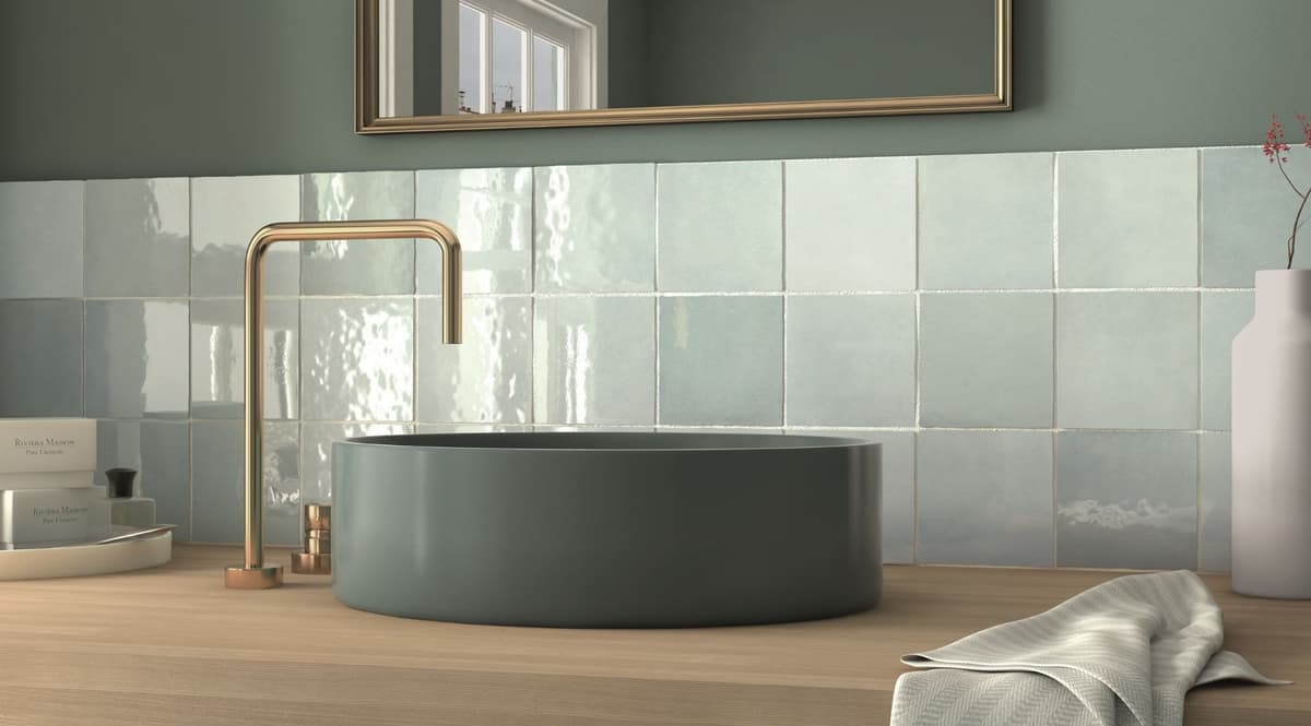 Zellige bleu pâle et nuancé 15x15 cm dans une salle de bain tons verts et bois avec lavabo rond et robinet cuivre