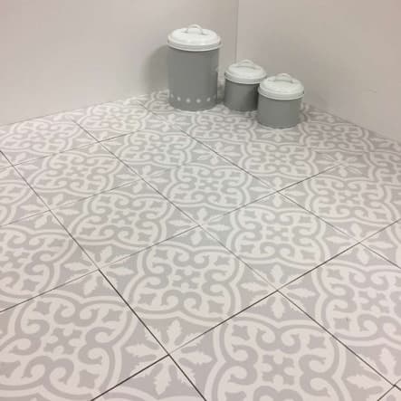 Carreau de ciment gris à motifs blancs 20x20 cm dans une pièce aux murs blancs avec trois pots décoratifs sur le sol