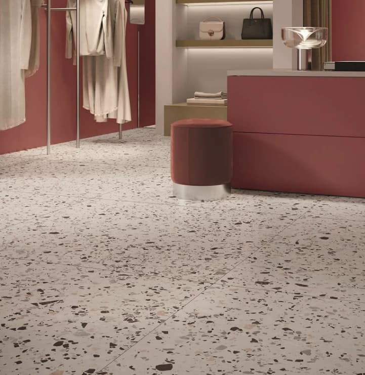 Carrelage Terrazzo blanc éclats multicolores 60x60 cm dans boutique mode murs rose tabourets ronds brun