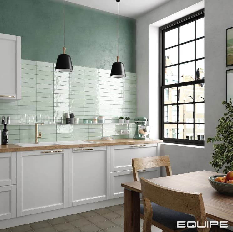 Carrelage Zellige vert lustré sur un mur de cuisine moderne blanc avec des touches de bois et des suspensions noires