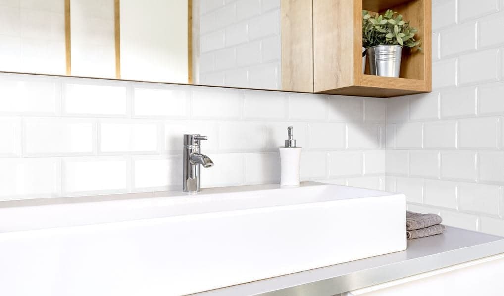 Carrelage uni blanc sans motifs 10x20 cm dans une salle de bain avec éléments bois et métal, lavabo moderne et accessoires blancs