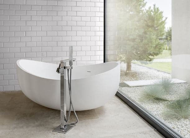 Carrelage uni blanc 10x20 cm dans une salle de bain moderne avec baignoire ovale, sol béton et vue sur jardin