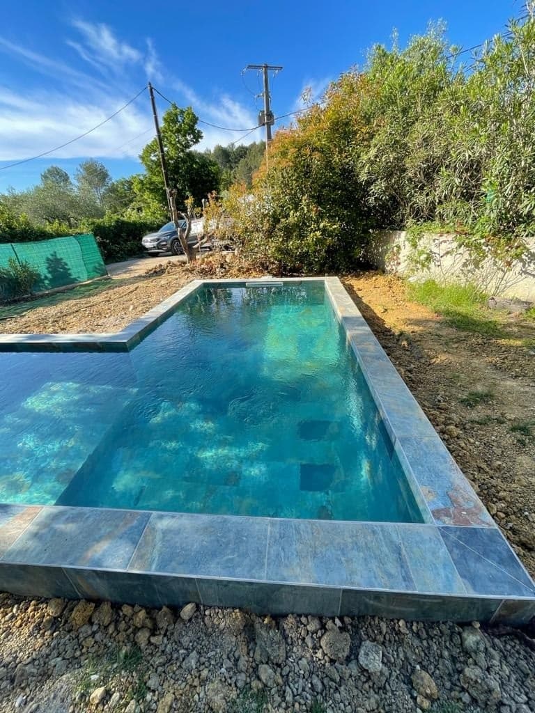 Carrelage pierre multicouleur nuances de gris et bleu 30x60 cm sur bord de piscine extérieure entourée de végétation