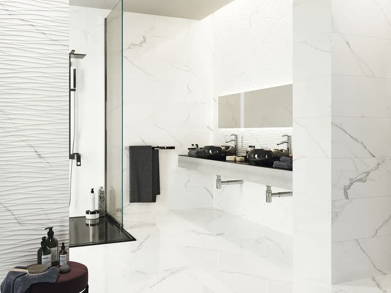 Carrelage blanc marbré sans motifs dans une salle de bain moderne, sur le sol et les murs, avec douche et lavabos noirs