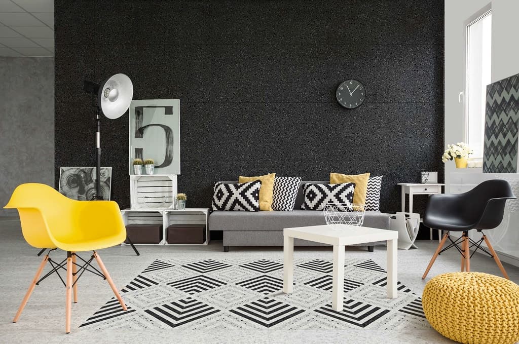 Carrelage Terrazzo beige nuancé dans un salon moderne avec murs noirs, un canapé gris, fauteuils jaune et noir, et décorations assorties