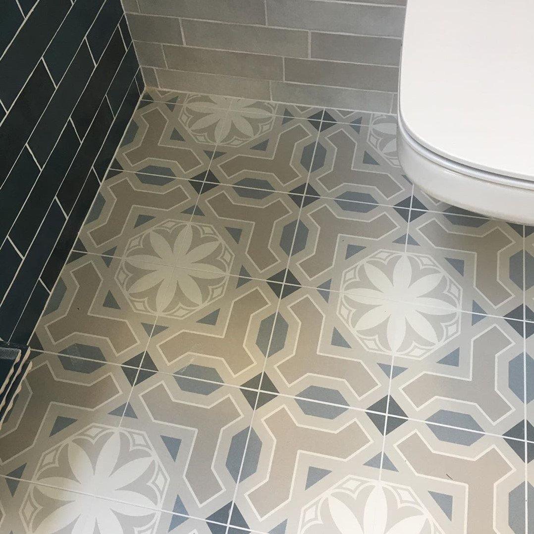 Carreau de ciment multicouleur motifs géométriques et floraux 20x20 cm dans salle de bains gris clair et blanc avec toilette et mur carrelé