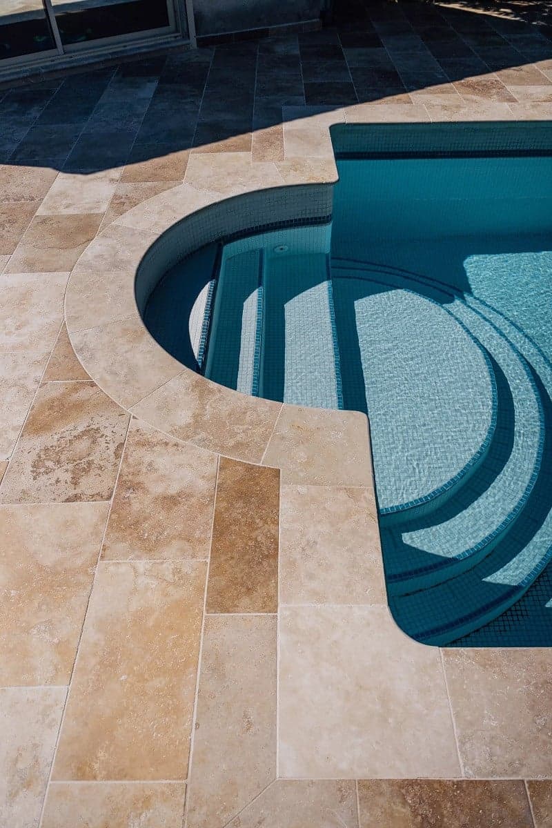 Carrelage aspect pierre beige nuancé sans motifs sur terrasse extérieure autour piscine bleue avec rebords arrondis