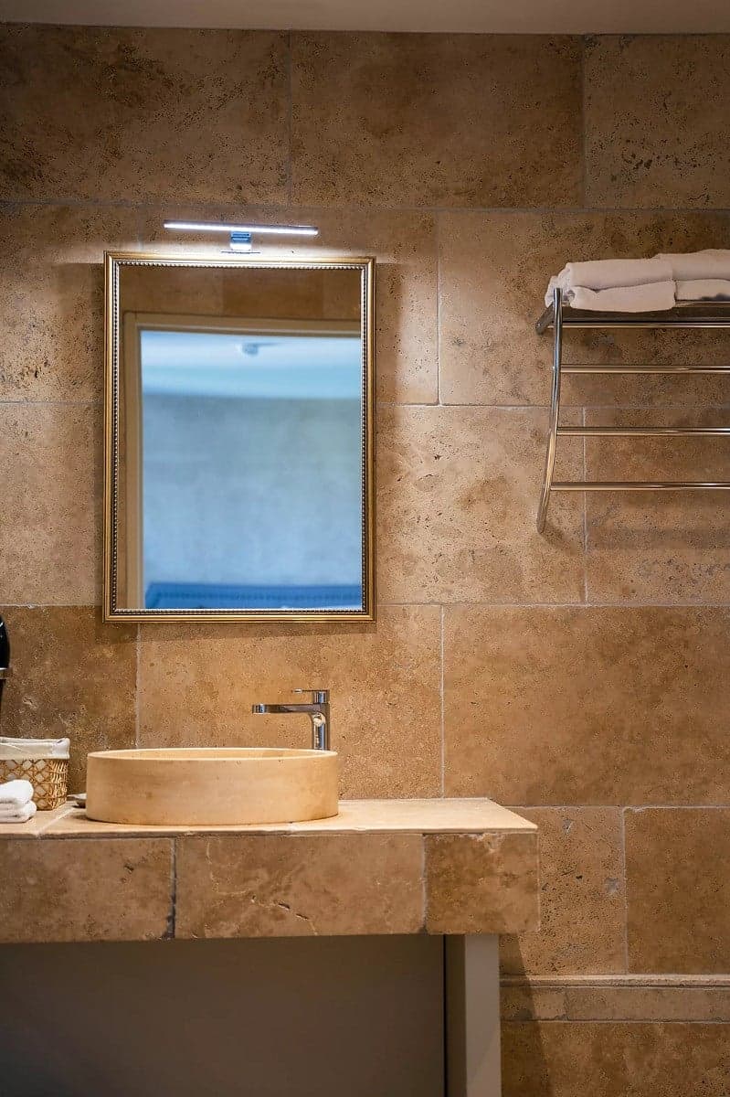 Carrelage pierre beige nuancé dans une salle de bain ton sur ton avec vasque, miroir et serviettes chauffées
