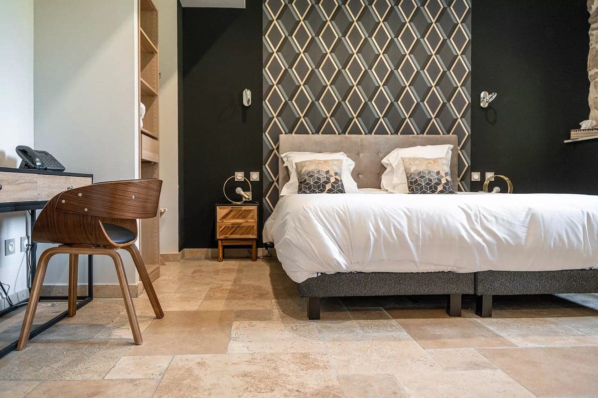Carrelage aspect pierre beige nuancé sans motifs dans une chambre avec murs noir et décor géométrique, mobilier bois et lit double