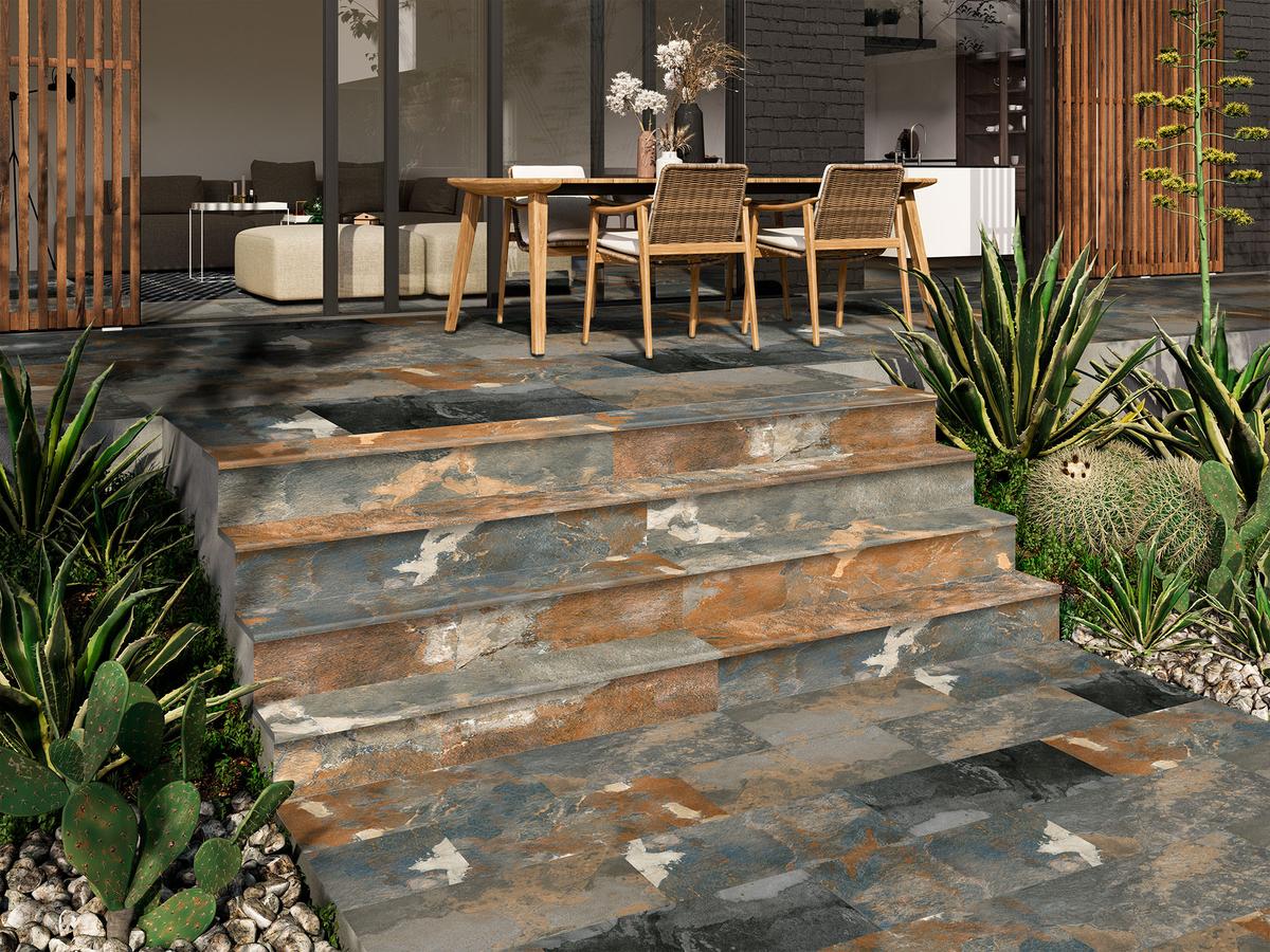 Carrelage effet ciment gris nuancé de marron et docres sur terrasse extérieure avec mobilier en bois et plantes vertes
