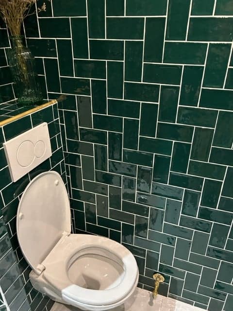 Carrelage uni vert 7,5x15 cm sur les murs de la salle de bain, combiné avec des sanitaires blancs et des éléments dorés
