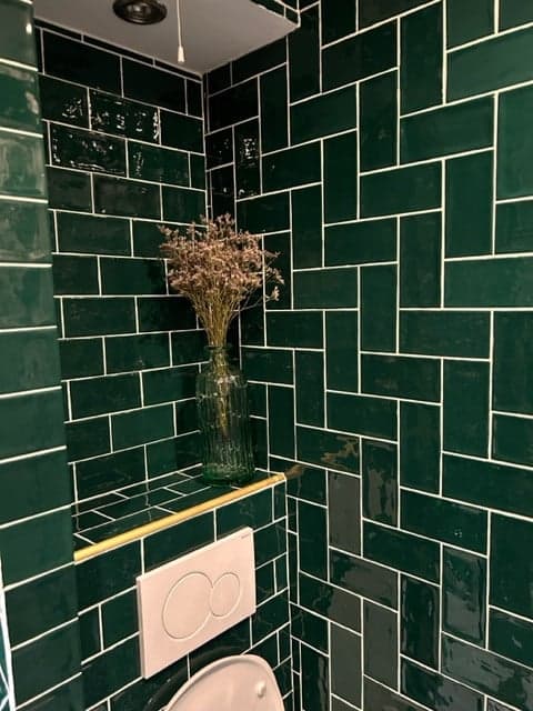 Carrelage uni vert émeraude brillant 7,5x15 cm sur un mur de salle de bain blanche avec vase et fleurs séchées