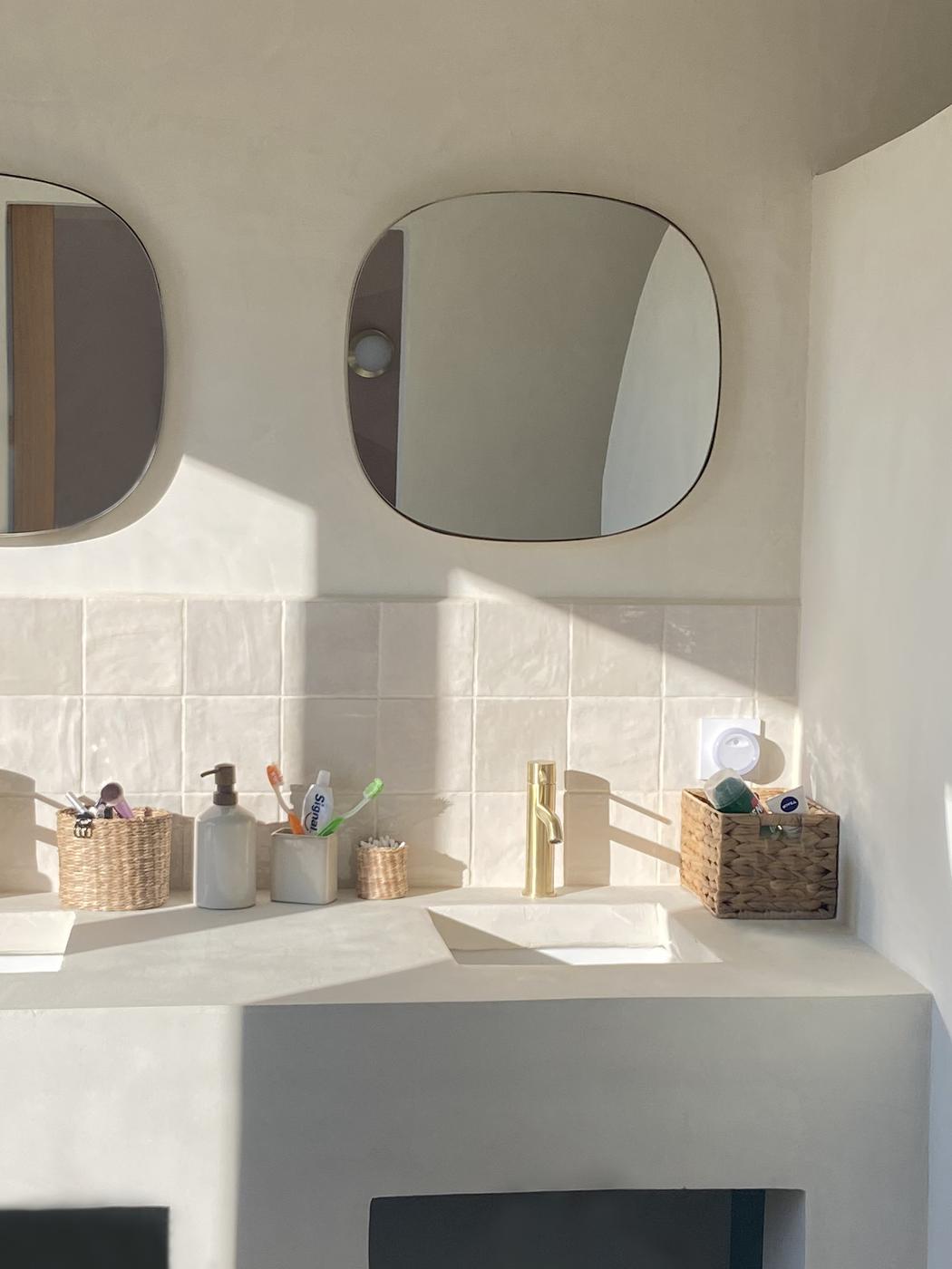 Carrelage Zellige blanc lisse 10x10 cm sur un plan de toilette beige avec miroirs ronds et accessoires de salle de bain