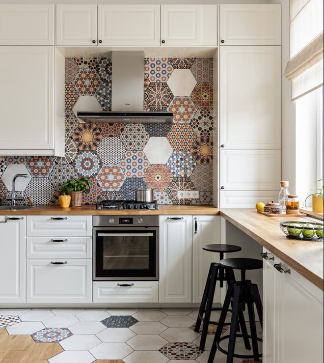 Carreau de ciment coloré terracotta motifs variés 30x30 cm dans une cuisine blanche avec plans en bois et tabourets noirs