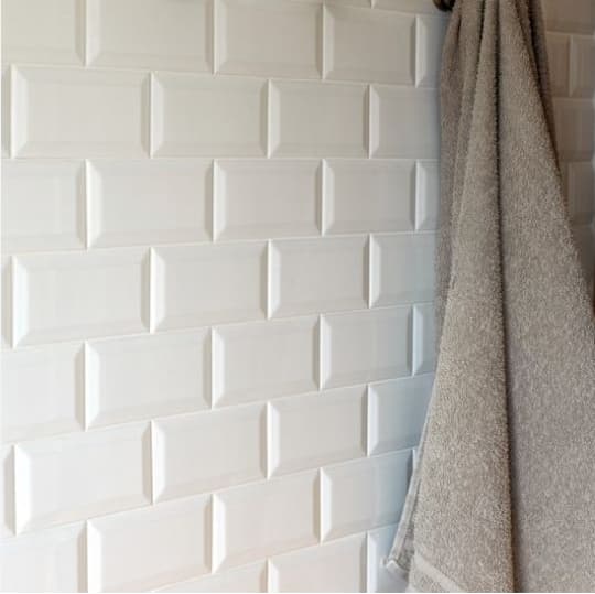 Carrelage uni blanc en relief sur un mur avec serviette grise accrochée dans une salle de bain aux tons neutres