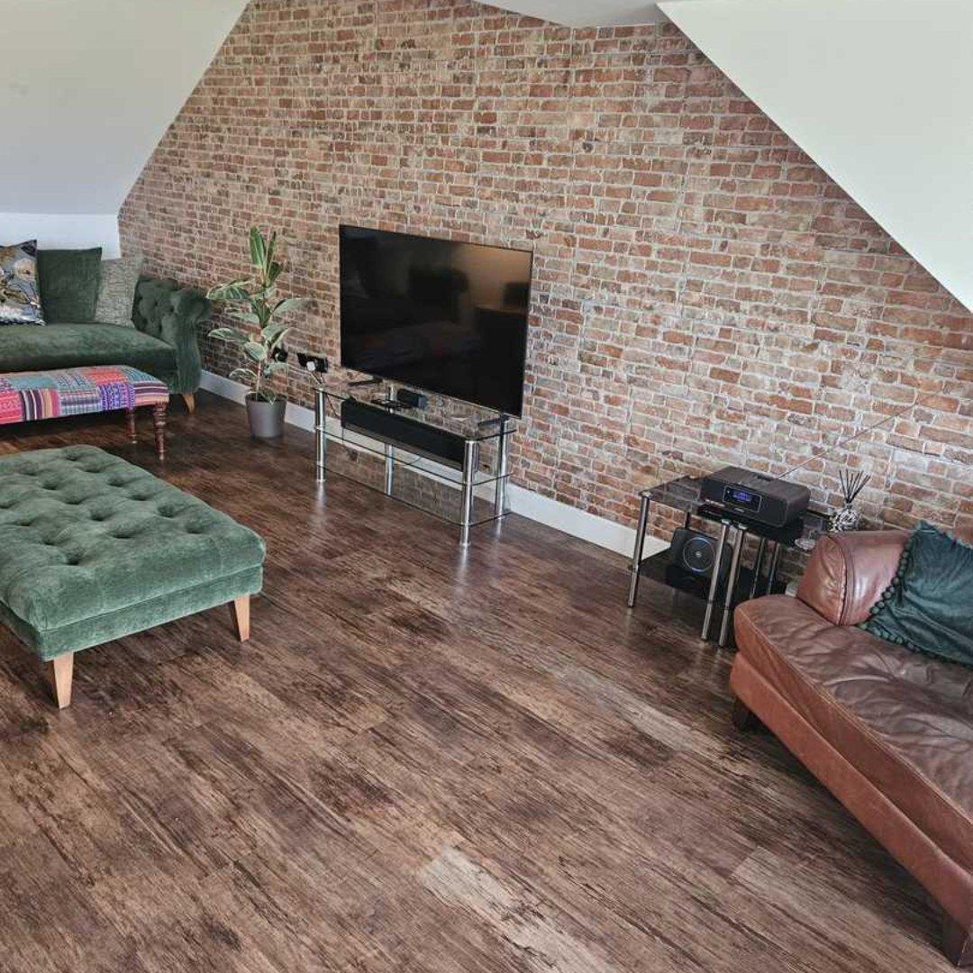 Carrelage effet bois terracotta dans un salon avec mur en briques apparentes, mobilier vert et marron, éclairage naturel