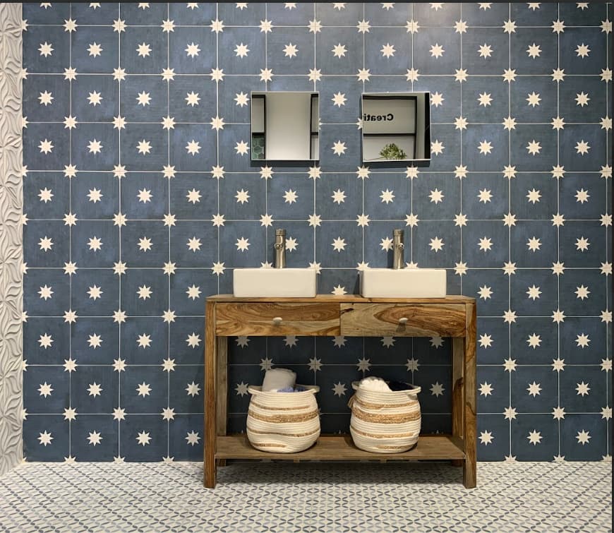 Carreau de ciment bleu à motif étoile blanc dans une salle de bain, murs et sol assortis, meuble en bois avec vasques, paniers en osier