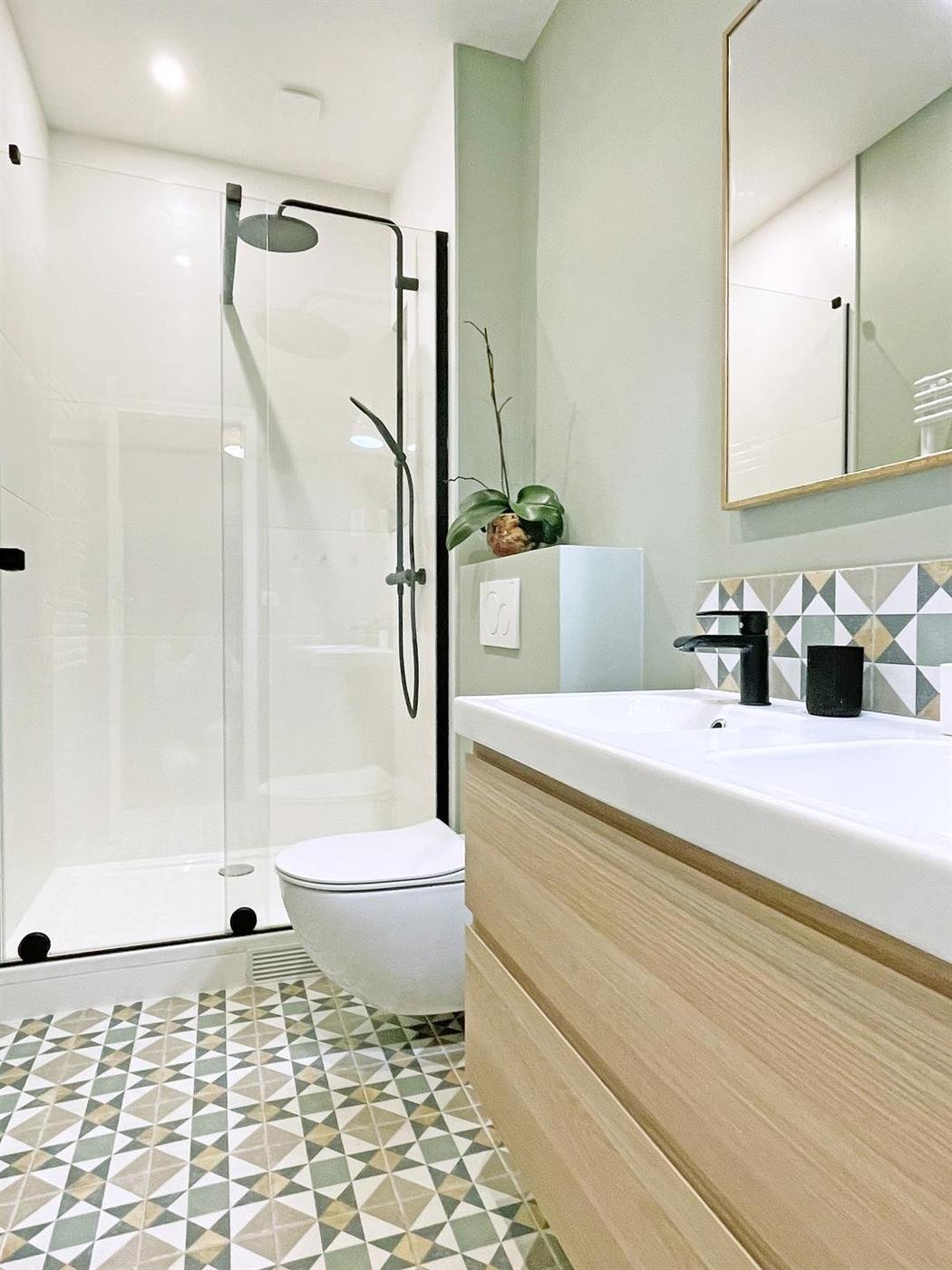 Carreau de ciment vert motifs géométriques 20x20 cm dans une salle de bain moderne tons pastels avec meubles en bois clair et détails noirs