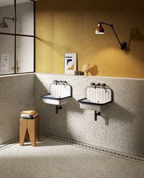 Carrelage Terrazzo blanc avec éclats colorés 20x20 cm dans une salle de bains aux murs ocre, avec vasques blanches, miroir, luminaire mural