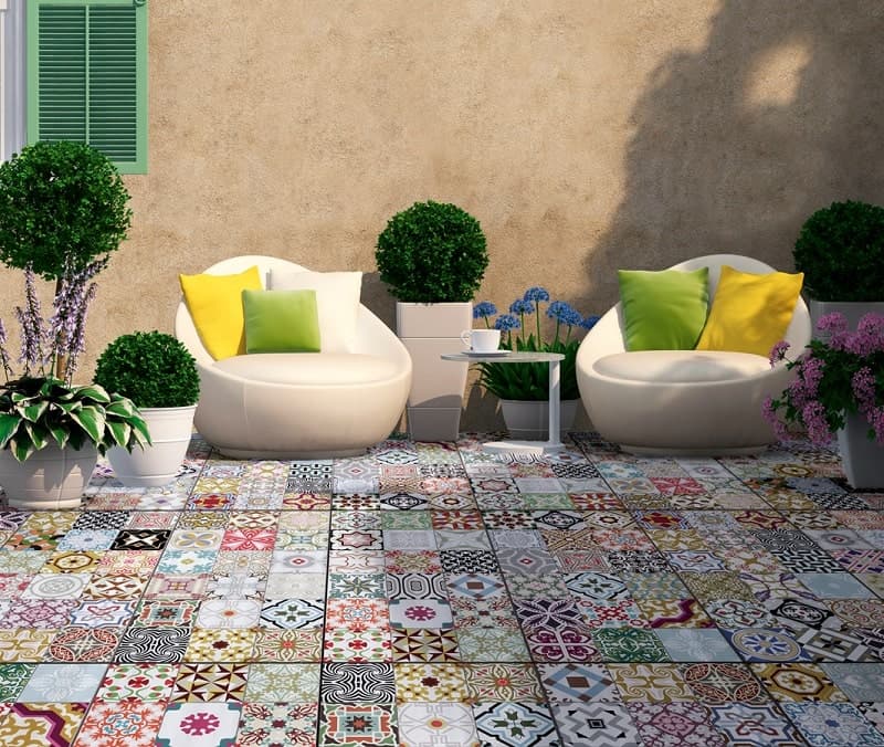 Carreau de ciment terracotta avec motifs variés sur terrasse extérieure beige fauteuils blancs coussins colorés plantes vertes