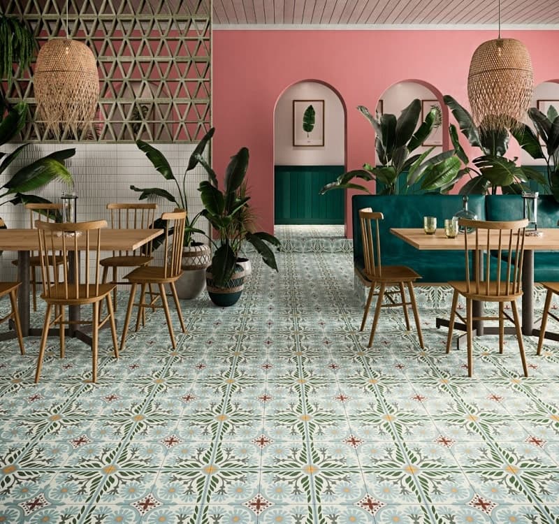 Carreau de ciment multicouleur à motifs floraux 60x60 cm dans une salle à manger avec murs roses et verts, mobilier en bois, plantes vertes