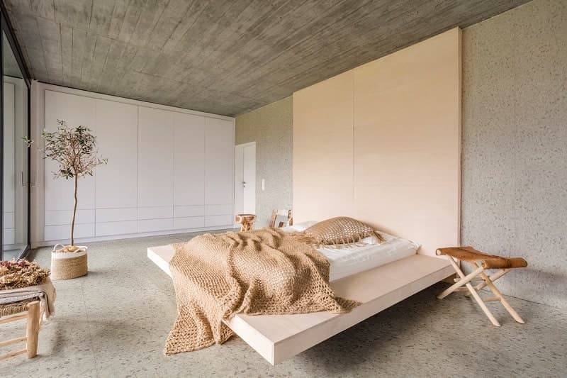 Carrelage Terrazzo beige avec nuances gris clair 60x60 cm dans une chambre minimaliste aux murs blancs et plafond en béton, éclairée naturellement