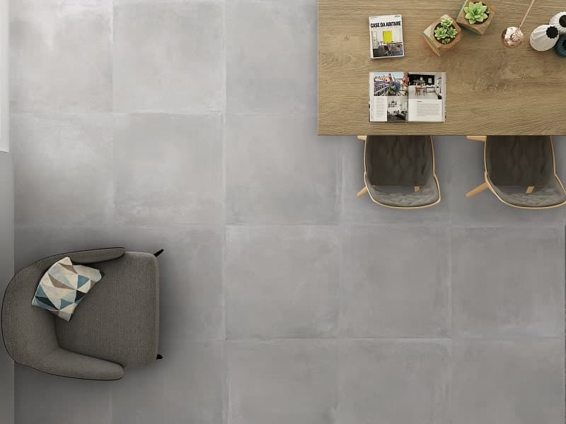 Carrelage effet béton gris lisse 60x60 cm dans un salon avec mur bois clair, fauteuil moderne et décoration minimaliste