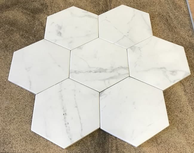 Carrelage aspect marbre blanc avec veines grises, forme hexagonale, sur fond beige.