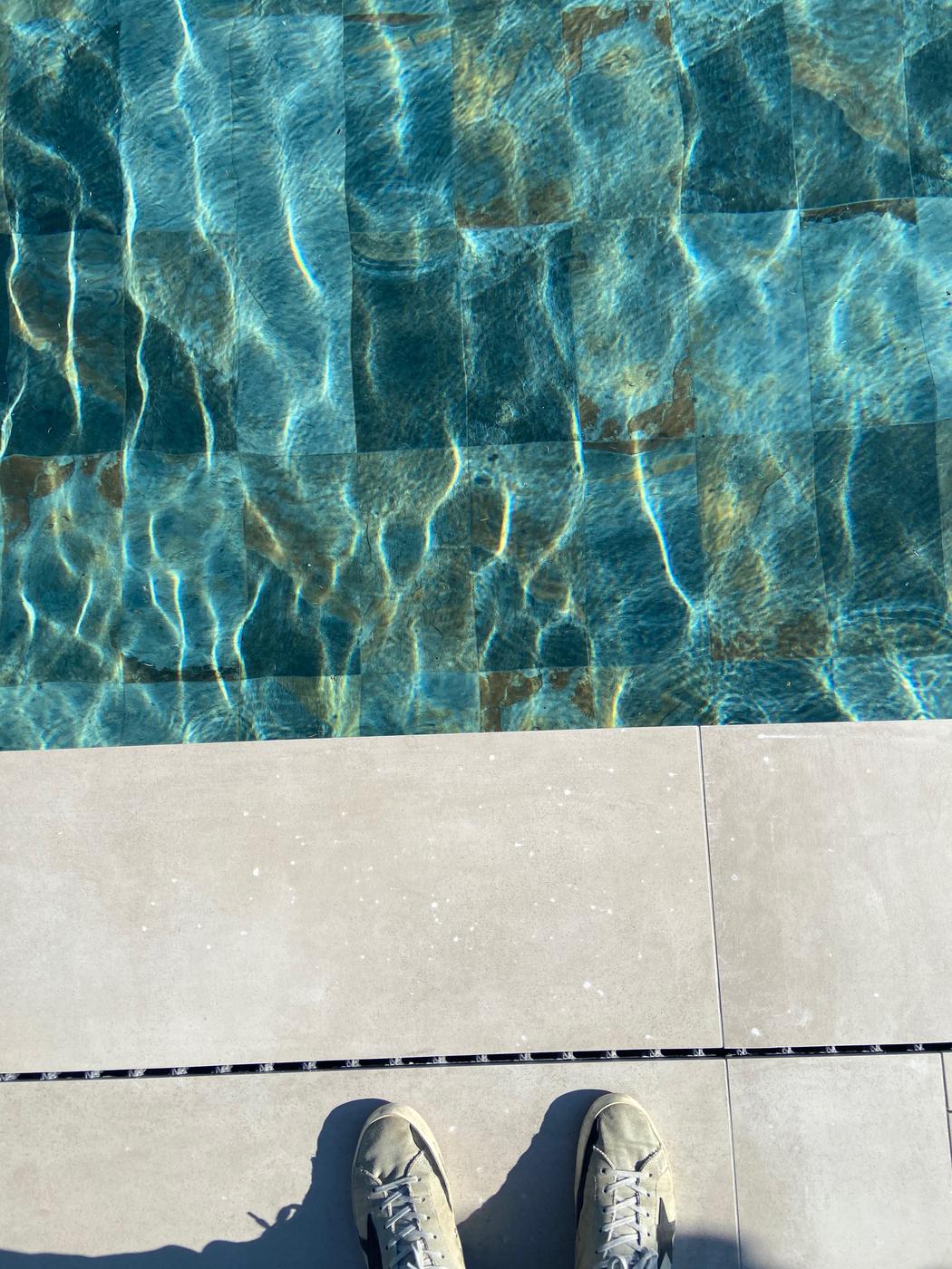Carrelage effet pierre multicouleur 30x60 cm sur bord de piscine aux eaux bleues cristallines et carrelage adjacent béton clair