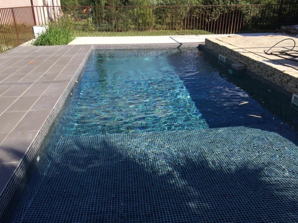Carrelage uni noir 30x30 cm dans une piscine extérieure eau bleue entourée de verdure